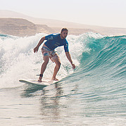 Élève en surf glissant sur une vague verte à Fuerteventura Tu glisses avec fluidité sur une vague verte – plein d’équilibre et de plaisir.